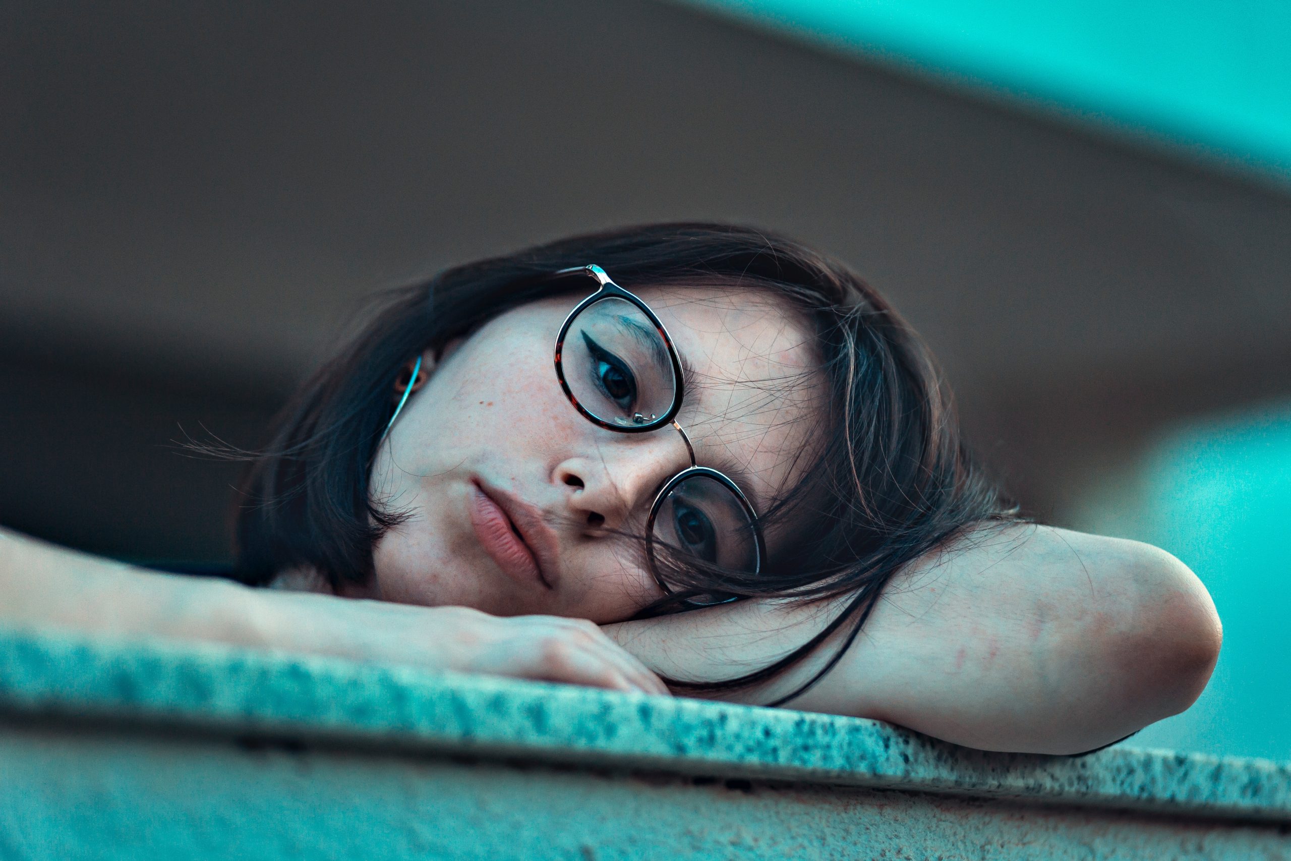Woman in eyeglasses laying on her arm due to boredom. Struggling with anxiety, procrastination or depression. Get online counseling in Ohio 44122 to overcome feelings of laziness, frustrations dealing with COVID-19, stay-at-home, sheltering in place and developing cabin fever.